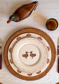 a plate with two birds on it next to some forks and spoons in front of a wooden duck