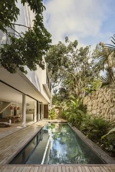 an outdoor swimming pool surrounded by greenery and wooden decking, next to a stone wall