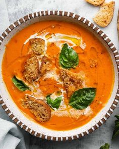 a bowl of tomato soup with bread and basil leaves on the side, ready to be eaten