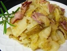 a white plate topped with potatoes covered in ham and onions next to a sprig of rosemary