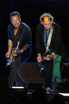 two men playing guitars on stage with one wearing a clown hat and the other holding an electric guitar