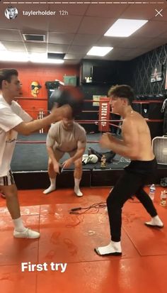 two young men practicing boxing in an orange gym room with one man standing up and the other sitting down