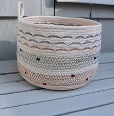 a white basket sitting on top of a wooden table next to a window sill