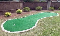 a miniature golf course in the backyard with grass and shrubs around it, next to a wooden fence