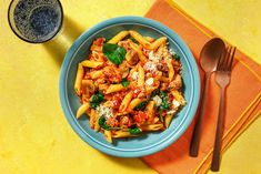 a blue bowl filled with pasta and meat on top of a yellow place mat next to a fork