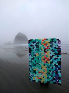 a person holding up a quilt on the beach