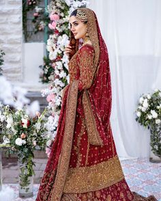 a woman in a red and gold bridal gown standing next to a floral arch