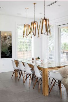 a dining room table with chairs and lights hanging from it's ceiling, in front of large windows