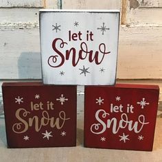 three red and white wooden signs that say let it snow