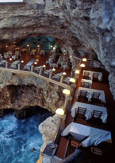 an outdoor restaurant with tables and chairs next to the ocean in a cave like setting