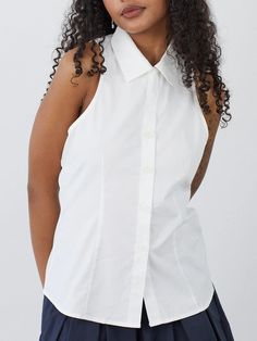 a woman with curly hair wearing a white shirt and navy blue skirt is looking at the camera