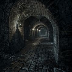 a dark tunnel with cobblestones and light at the end