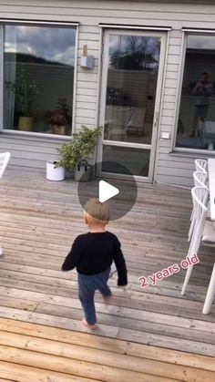 a little boy walking across a wooden deck next to a white table and chair set