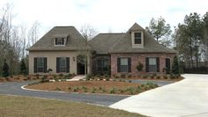 a large brick house with lots of windows and bushes in front of the driveway area