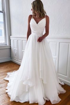 a woman in a white wedding dress standing on a wooden floor next to a window