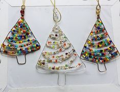 three christmas trees made out of glass beads and metal wire are hanging on a white board