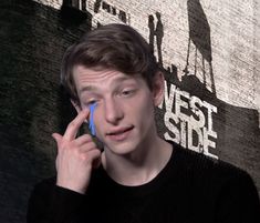 a man talking on a cell phone while standing in front of a wall with the words west side painted on it