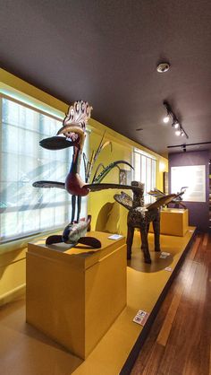 several sculptures are on display in a room with yellow walls and wood floors, along with wooden flooring