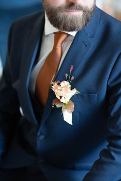 a man with a beard wearing a blue suit and flower boutonniere on his lapel