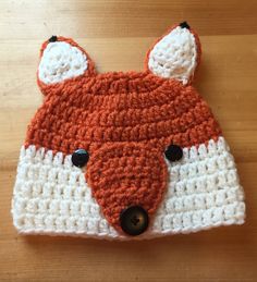 an orange and white knitted hat with a fox face on the front, sitting on top of a wooden table