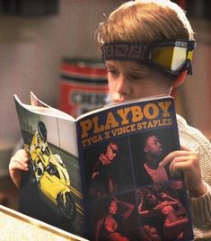 a young boy reading a book with goggles on his head