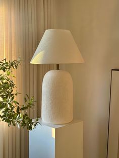 a white lamp sitting on top of a table next to a plant