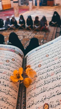 an open book with arabic writing and flowers on the pages, in front of other people