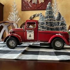 an old fashioned red truck with christmas trees in the back is sitting on a black and white checkered tablecloth