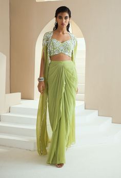 Editor's Note Draped Jumpsuit With Embroidery On Waist, Neckline And Shoulder. Fabric: Choli And Skirt- Georgette, Cape- Organza, Satin Lining Color: Green Embroidery Details: Hand Embroidery With Zari, Pearls, Glass Beads And White Beads. Care: Dry Clean Only About the Designer Seema Thukral collection offers glamorous, elegant, and chic clothing for women. It consists of drapes with intricate handwork and embroideries. The brand forte is all about different and unique cuts that involve a lot o Draped Skirt With Cape, Drape Skirt Outfit Indian, Cape And Skirt Outfit, Skirt With Blouse Outfit, How To Make Drape Skirt, Draped Skirt Outfit, Indowestern Skirt, Dhoti Skirt Outfits, Drape Skirt Indian