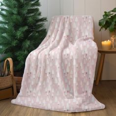 a pink and white blanket sitting on top of a wooden floor next to a christmas tree