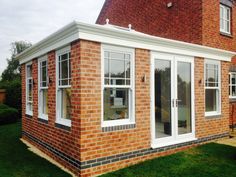 a red brick house with white windows and an extension to the back wall, in front of a green lawn