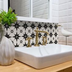 a white sink sitting under a bathroom mirror next to a vase with a plant in it