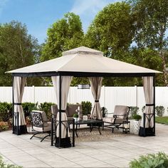 a gazebo sitting on top of a patio next to a white fence and trees