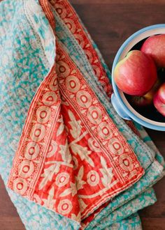 a bowl of apples sitting on top of a table next to a teal cloth