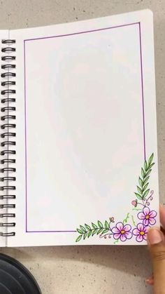 a hand holding a spiral notebook with flowers on the cover and blank paper attached to it