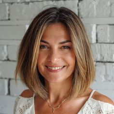 a woman with blonde hair smiling and wearing a white top in front of a brick wall