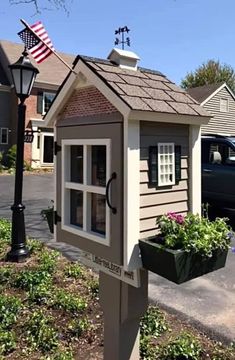 a small wooden house with an american flag on the roof and flowers growing in it