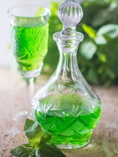 a green drink in a glass next to a decanter with leaves on it