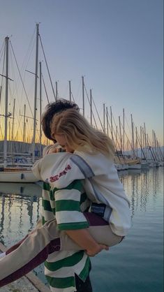 a woman carrying a child on her back near the water with sailboats in the background