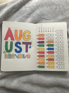 an open book with the words august written in colorful letters on it, sitting on top of a gray blanket