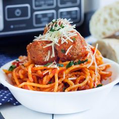 spaghetti and meatballs with parmesan cheese in a white bowl on a table