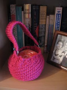 a pink crocheted basket sitting on top of a book shelf next to books