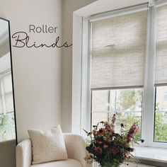 a white chair sitting in front of a window next to a vase filled with flowers