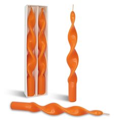 an orange candle is in a box and next to it's long, twisted candles