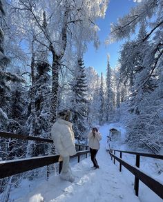 two people standing on a snowy path in the woods, one is wearing a white coat