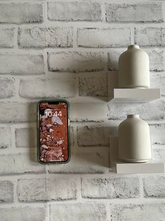 two white shelves and one with a cell phone on it in front of a brick wall