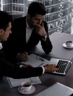 two men sitting at a table with laptops and papers in front of their faces