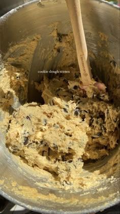 a metal mixing bowl filled with batter and chocolate chip cookie dough, with a wooden spoon in it