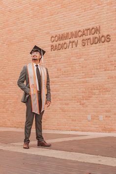 a man standing in front of a brick building wearing a graduation cap and gown with his hands on his hips