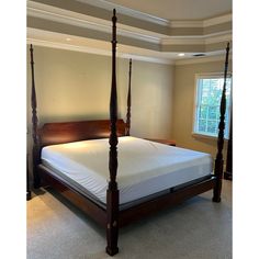 a four post bed with white sheets and pillows in a large room that has carpeted flooring